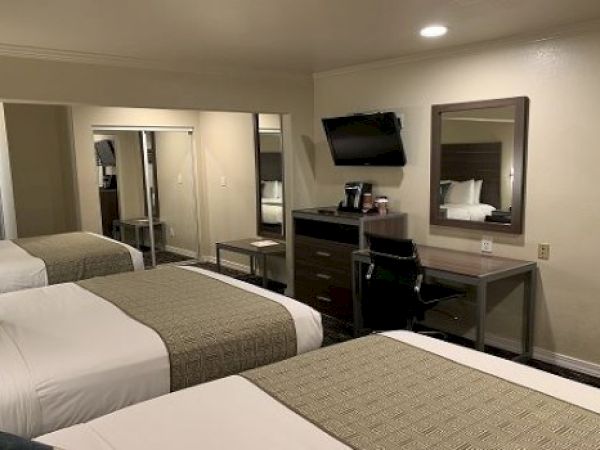 A hotel room with two double beds, a desk, wall mirror, mounted TV, and neutral beige walls, plus a dresser and mirrored closet.