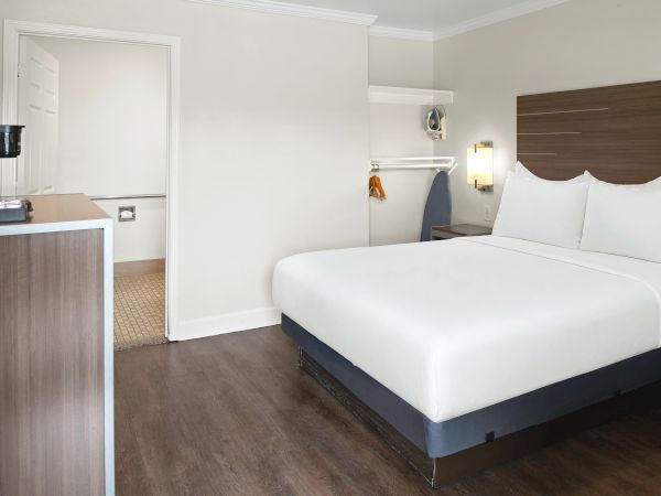 A modern hotel room with a large bed, white pillows, wall lamp, and a view into a bathroom with sink and door.