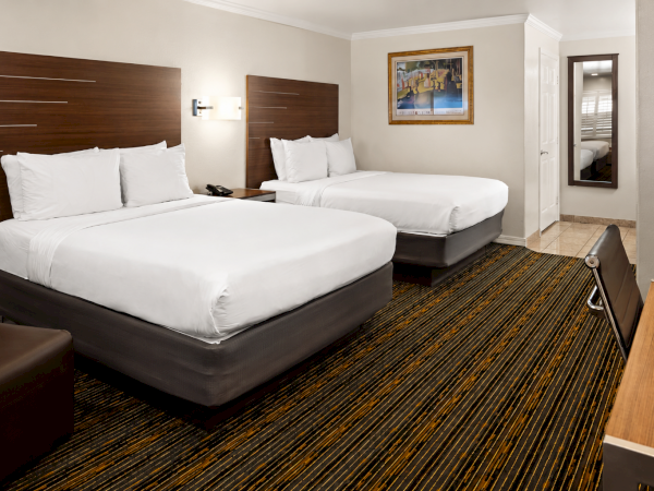 A bright hotel room with two neatly made beds, dark wood headboards, and a patterned carpet.