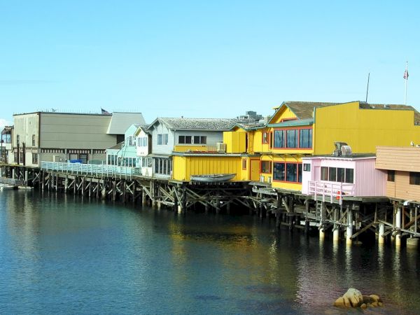 Colorful houses on stilts along a calm harbor, pastel blues, yellows, and pinks lining the water&rsquo;s edge.