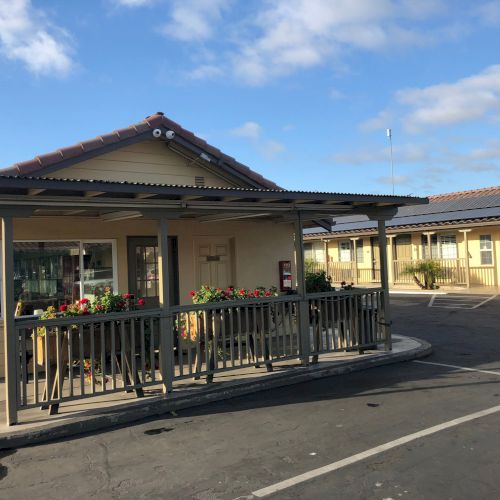 Old-fashioned porch train station with a single platform, yellow building, and steel tracks under a partly cloudy sky.