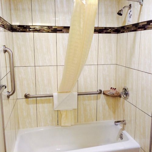 A beige-tiled bathroom with a shower curtain partially pulled across, a grab bar, a towel rack, and a bathtub with a handheld shower head.