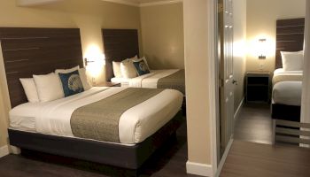 A hotel room with two large beds, nightstands, lamps, neutral decor, and a doorway leading to a small sitting area or ensuite.