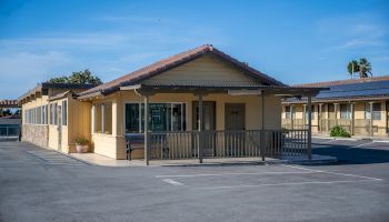 A lone, single-story motel with beige walls, a covered entrance, and a spacious parking lot under a blue sky.