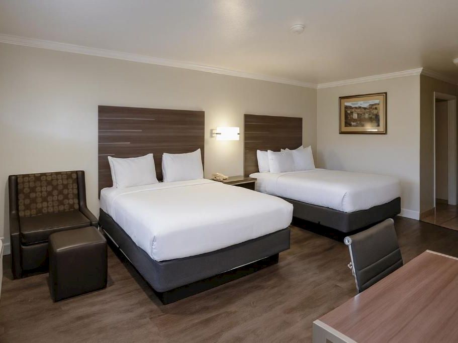 Two queen beds with white linens, a small seating area, a desk, and a chair in a modern hotel room.