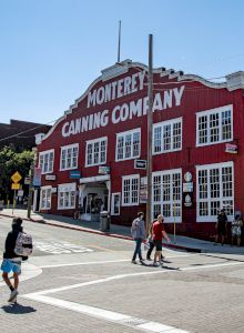 A red row of vintage-style buildings on a sunny street, people walking, and mountains in the background.